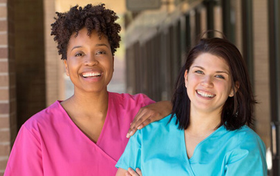 two smiling women in scrubs looking at camera two smiling women in scrubs looking at camera