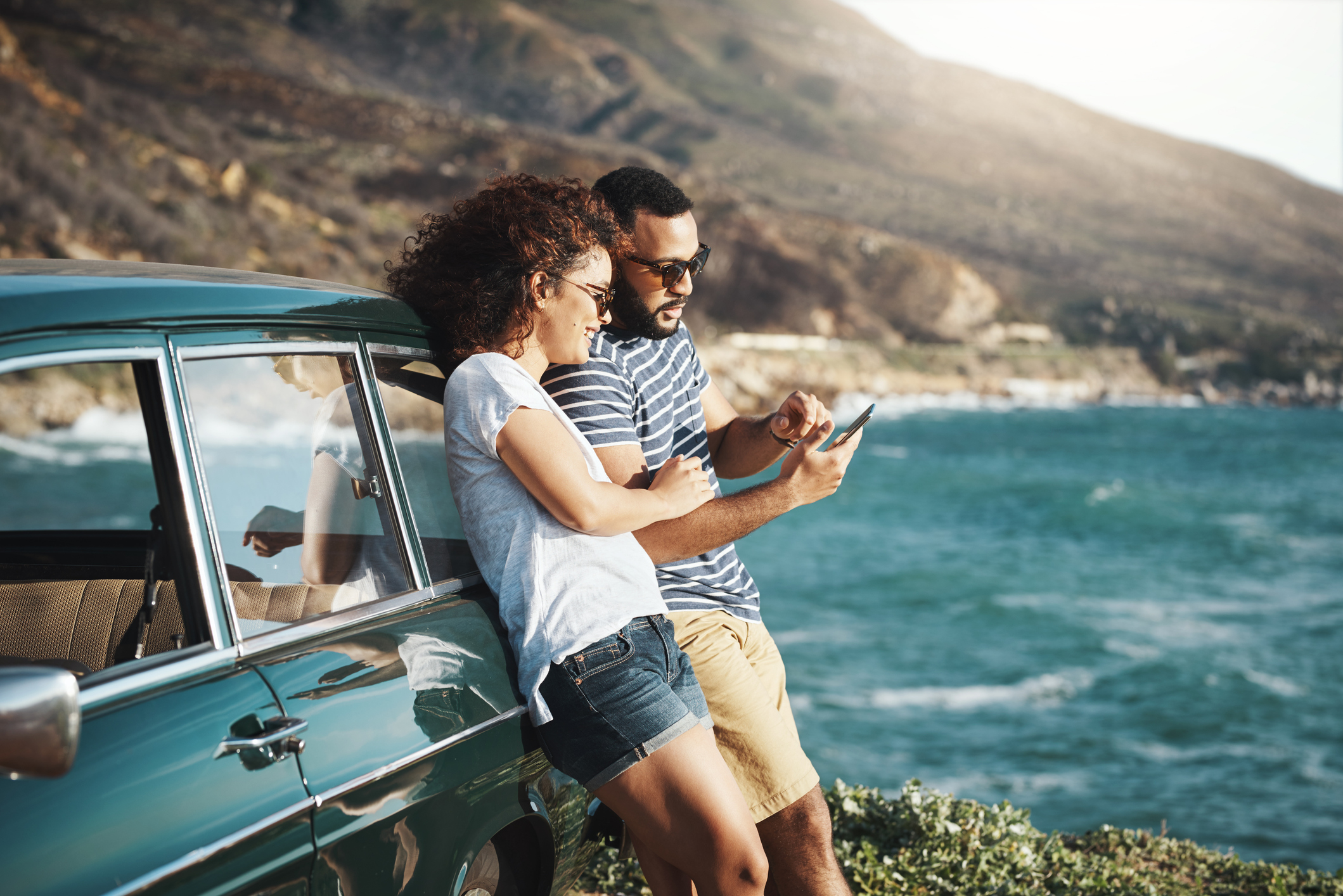Two happy individuals leaning against a car and looking at mobile device. Two happy individuals leaning against a car and looking at mobile device.