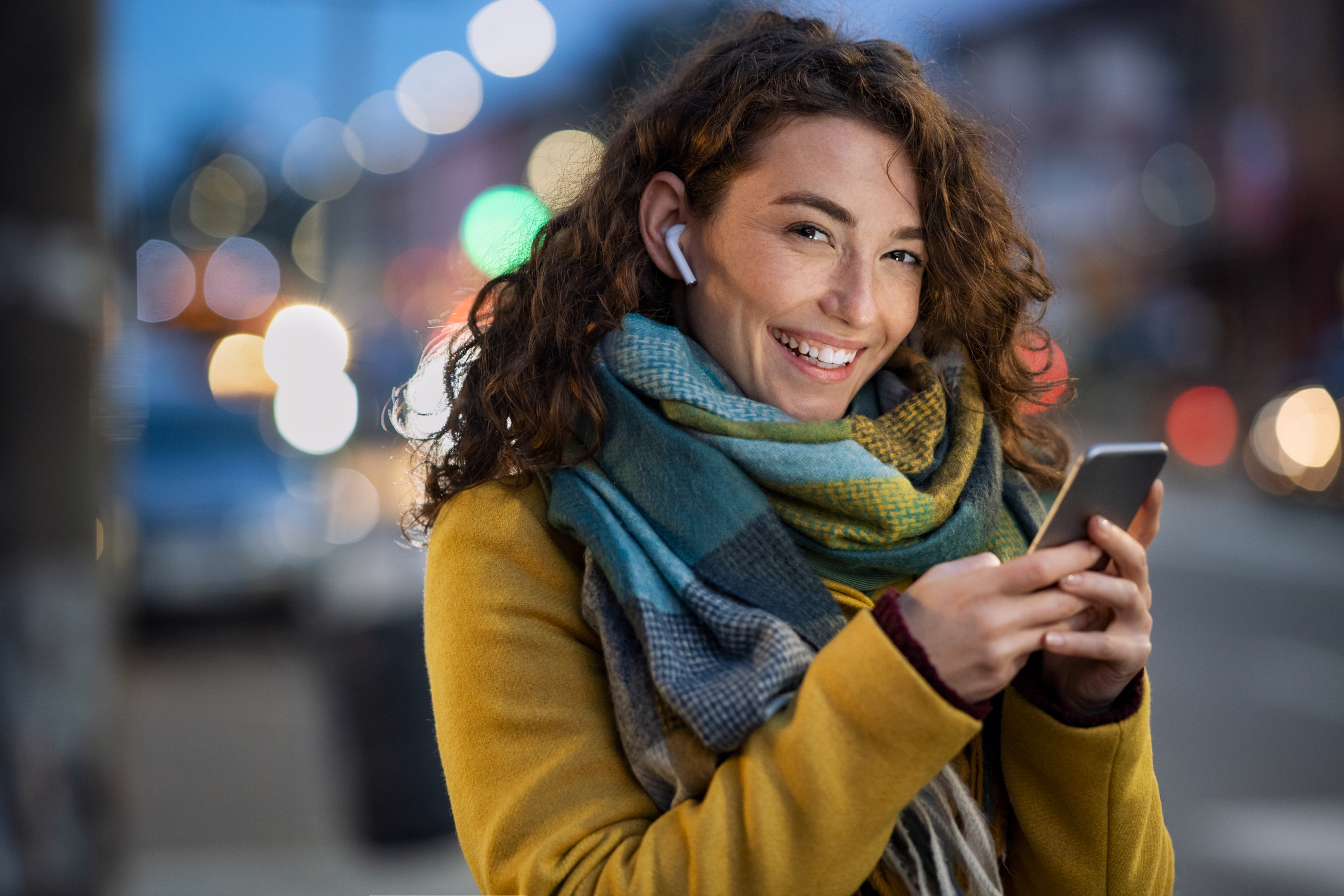 smiling woman wears air buds while holding mobile phone 