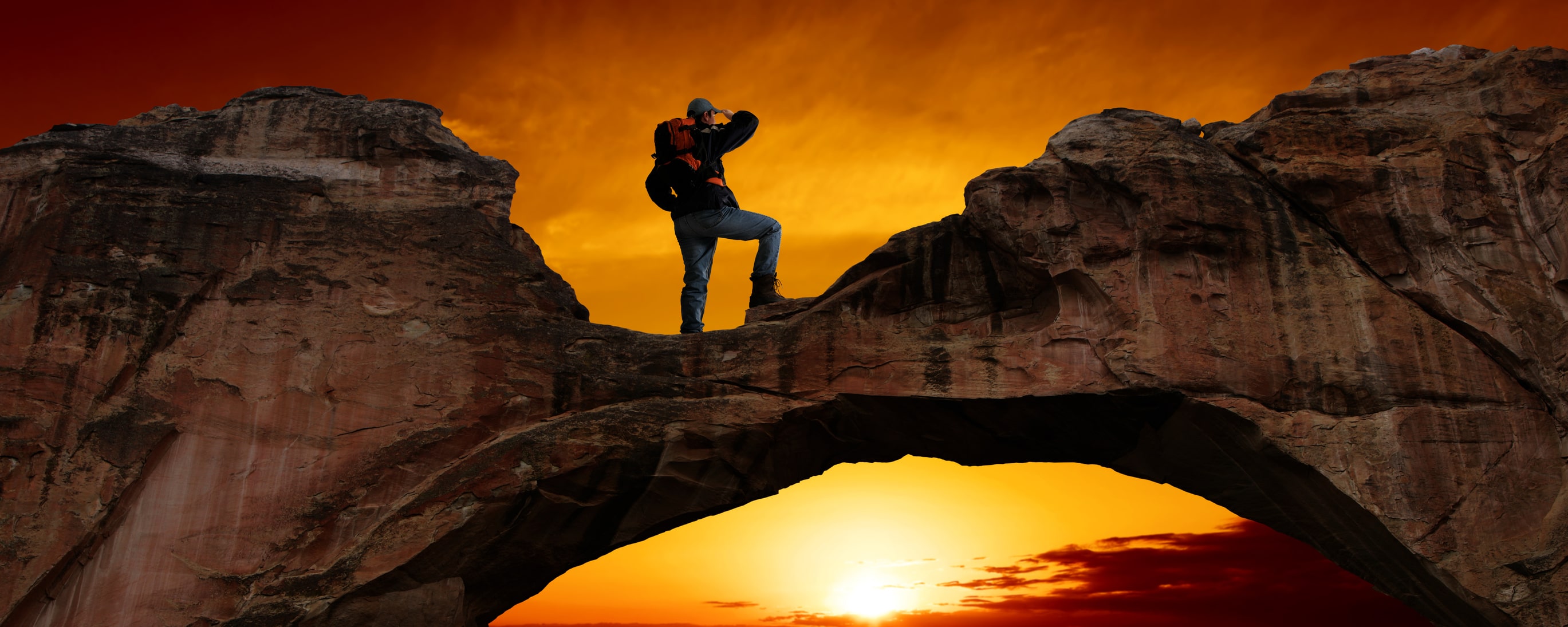 male hiker taking pictures from atop the center of a large rock formation in arizona desert at sunset, where round cut-out formed in rock