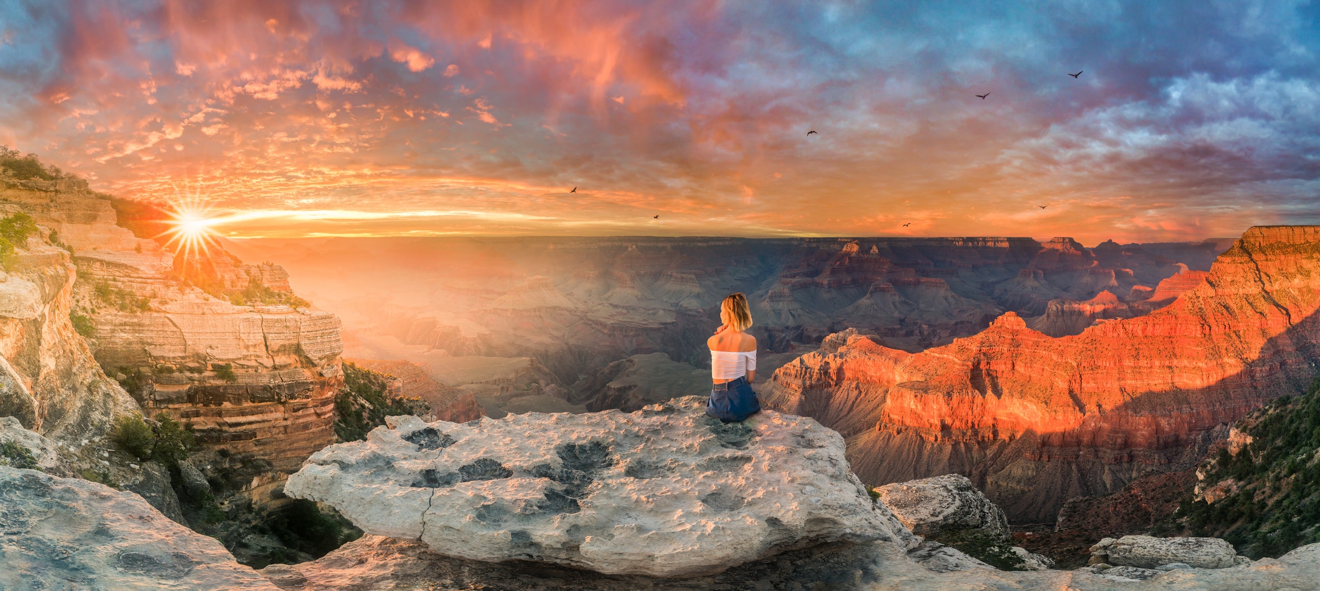blonde woman in white top and shorts, sitting on  huge rock formation, overlooking grand canyon 